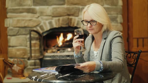 Une femme avec un verre de vin rouge se repose au restaurant. Regarde le magazine sur la table — Video