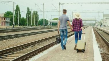Çanta ile genç bir çift istasyonunda platformda gider. Yeni evliler balayına gitmek. Arkadan Görünüm