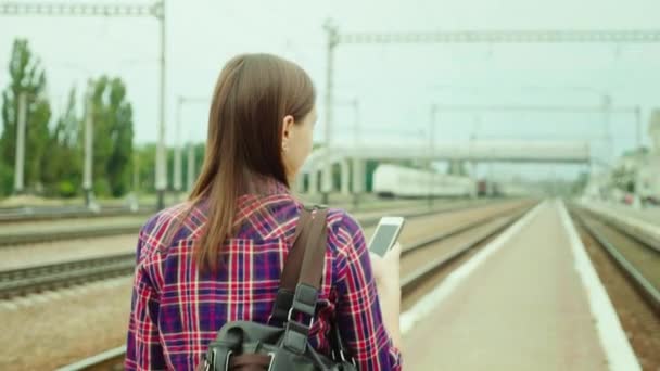 リアを見よ: ハンサムな若い女性が鉄道プラットフォームに沿って行きます。携帯電話を使用しています。概念は成功するビジネス旅行です。 — ストック動画