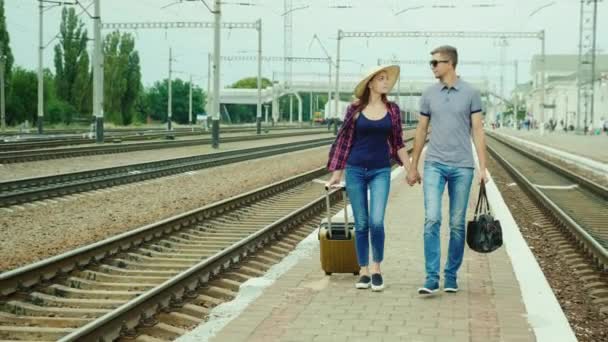 Молодая пара с сумками идет на платформу на вокзале. У молодоженов медовый месяц. Вид спереди — стоковое видео