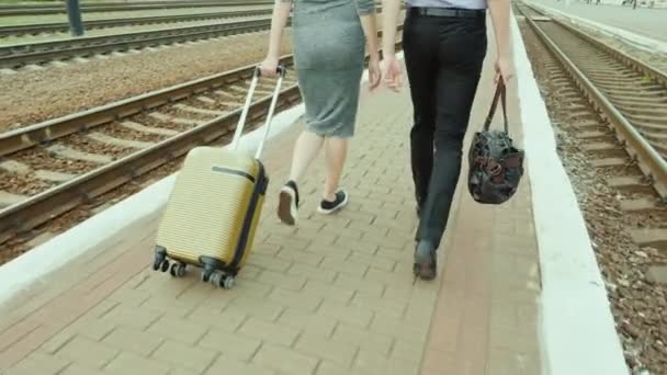 Two business people walk along the railway, with them their luggage. In the frame only the legs are visible. Steadicam shot, rear view