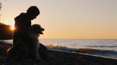Birlikte göl ya da deniz üzerinde gün batımını izlemek onun köpek yanında bir adam oturuyor