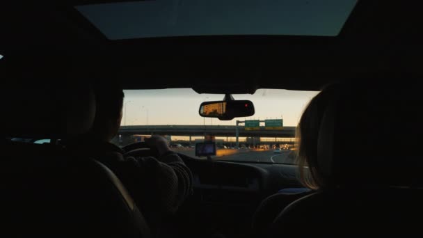 Pareja joven montando en un coche con una escotilla de cristal en la carretera — Vídeos de Stock