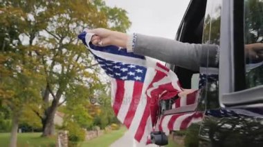 Bir adam büyük bir Amerikan bayrağı elinde tutar, onu hareket eden bir arabanın penceresinden pokes. Slow Motion video