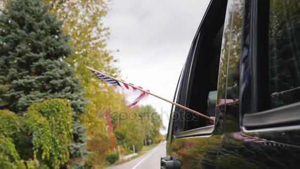 Una mano con una bandiera americana guarda fuori dal finestrino di una macchina da viaggio. Video al rallentatore — Video Stock