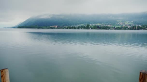 Une femme s'assoit sur une jetée en bois, regarde les montagnes et le lac de montagne dans le brouillard. Steadicam shot — Video