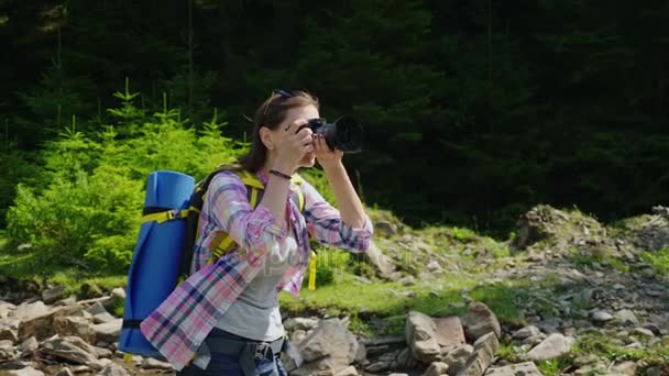 Uma fotógrafa fotografa a natureza. Em um lugar pitoresco no fundo de uma floresta perto de um rio de montanha. Estilo de vida ativo — Vídeo de Stock