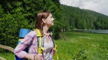 Genç turist kadın meadows, dağlar ve gökyüzü arka planda pitoresk bir yere gider. Turizm ve aktif yaşam tarzı