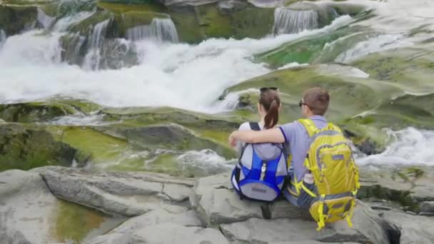 愛情のあるカップルは、美しい山川を賞賛します。彼らは岩の上に並べて座る、沸いて周り — ストック動画
