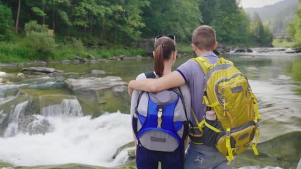 Um jovem casal admirando o rio da montanha. Homem abraçando sua namorada, visão traseira — Vídeo de Stock