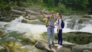 Genç bir çift kendilerini dağlarda bir şelale çerçevede fotoğraf çekme yolcuları. Vinç vurdu