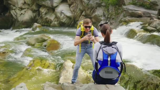 O marido tira fotos de sua esposa em um lugar pitoresco em um rio de montanha. Tempo feliz em conjunto, modo de vida ativo e saudável — Vídeo de Stock