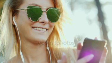 Bir akıllı telefon elinde tutan şık genç kadın kulaklıklar, müzik dinlemek.