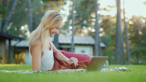 Atraktivní žena používá notebook. Sedí na trávníku v jeho dvoře — Stock video