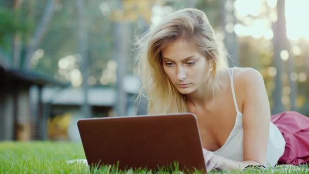 Jovem mulher sexy encontra-se no gramado, gosta de laptop — Vídeo de Stock