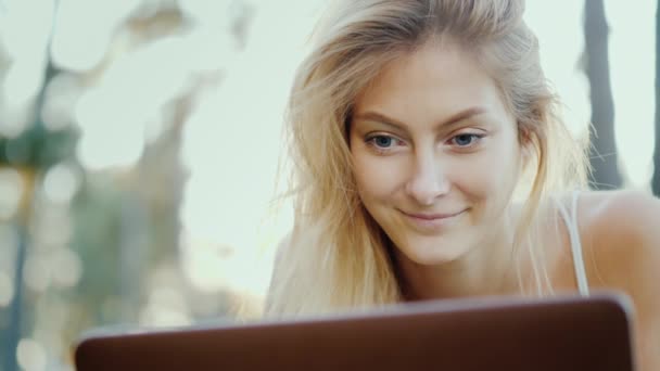 Porträtt av en ung kvinna som njuter av en bärbar dator. Lögner på gräsmattan, solen lyser vackert hennes hår — Stockvideo