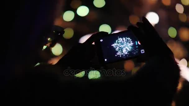 Una mujer admira los fuegos artificiales en el cielo nocturno. Toma fotos con tu smartphone. Vídeo de 4k 10 bits — Vídeo de stock