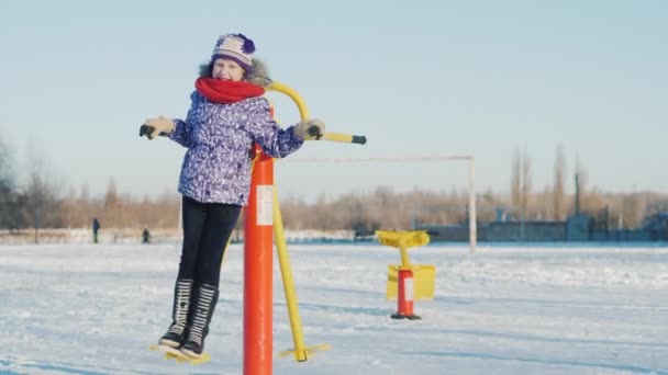 Une écolière roule sur une balançoire dans la cour d'école. Une journée d'hiver claire — Video