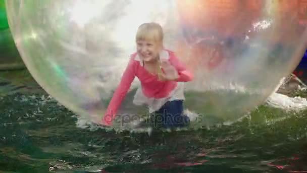 Dítě má zábavu, běží a spadá uvnitř průhledné koule, která plave ve vodě. Zábavný víkend v zábavním parku — Stock video
