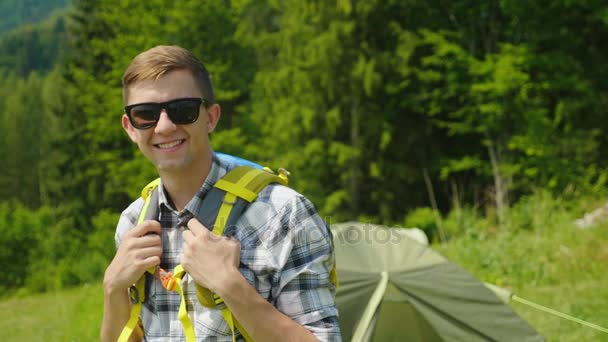 Portret szczęśliwy mężczyzna podróżnika. Uśmiecha się, patrząc na kamery, stojący w pobliżu namiot na campingu — Wideo stockowe