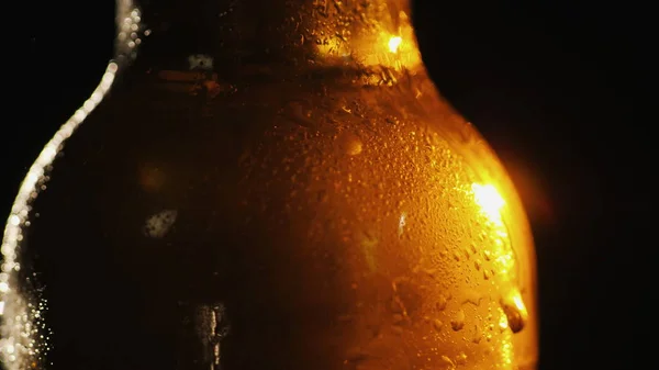 Una botella de cerveza fría sobre un fondo negro. Un rayo de luz lo ilumina maravillosamente — Foto de Stock