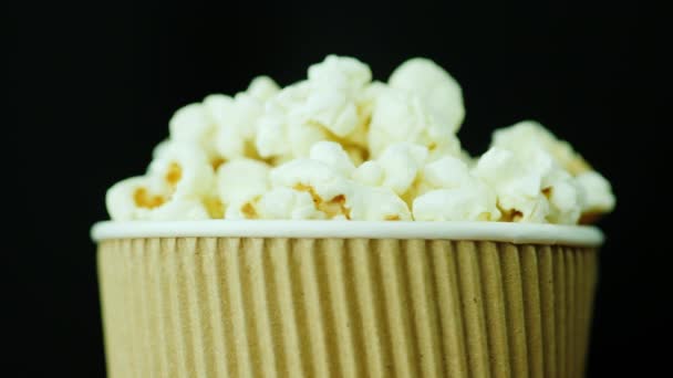 Un vaso de palomitas de maíz deliciosas. Rota suavemente sobre un fondo negro. Comida para ver películas . — Vídeos de Stock