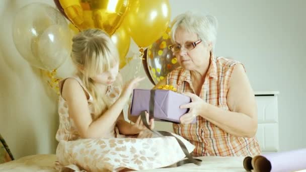 Embalagem de presentes para o aniversário. Uma mulher idosa com uma menina está embalando um presente juntos — Vídeo de Stock