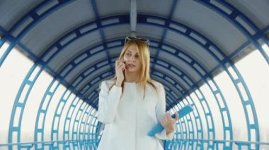 İş kadını telefonla konuşuyor. Hızlı bir şekilde iş merkezi cam tünelde geçer