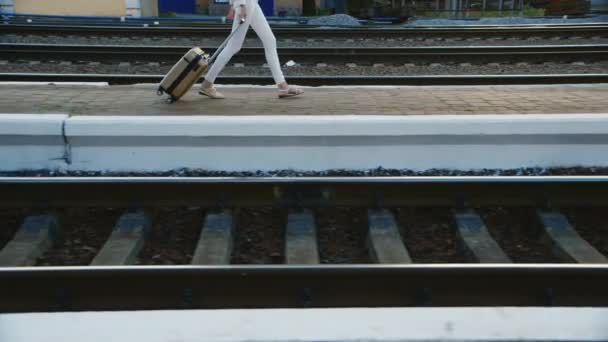 Kobieta w garniturze w podróżnej jest na stacji kolejowej. Na zdjęciu mogą być widoczne tylko nogi i torbę na kółkach — Wideo stockowe