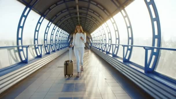 Steadicam geschoten: leven in beweging. Stijlvolle vrouw met reistas is zonovergoten onderweg tussen terminals — Stockvideo