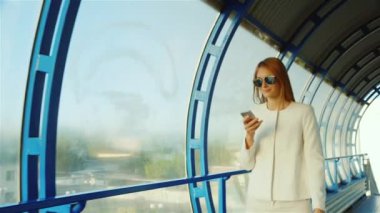 İş kadın tünel söz güneş ışığı ile sular altında. Telefon seyahat çantasında kullanın. Cam Havalimanı terminalleri arasında geçiş
