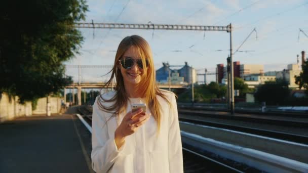 Une femme d'affaires marche le long de la gare à l'aide d'un téléphone intelligent. Communication dans le concept de voyage — Video