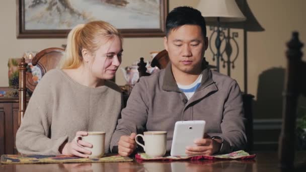 Familienfrühstück - ein Paar liest die Nachrichten auf dem Tablet, sitzt am Tisch im Esszimmer und trinkt Tee — Stockvideo