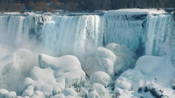 冷凍ナイアガラの滝の雄大な眺め。岩の間の水の流れは、氷と雪で覆われています。4 k 10 ビット ビデオ — ストック動画