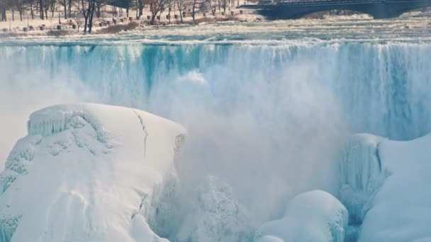 La belleza del invierno en las Cataratas del Niágara. Corrientes de agua caen sobre rocas heladas. Nieve blanca brilla en el sol — Vídeo de stock