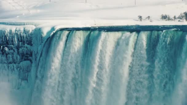 Idyllisk utsikt över vintern Niagara Falls. Jorden är täckt med ren snö, vattnet faller på stenar täckt med is — Stockvideo