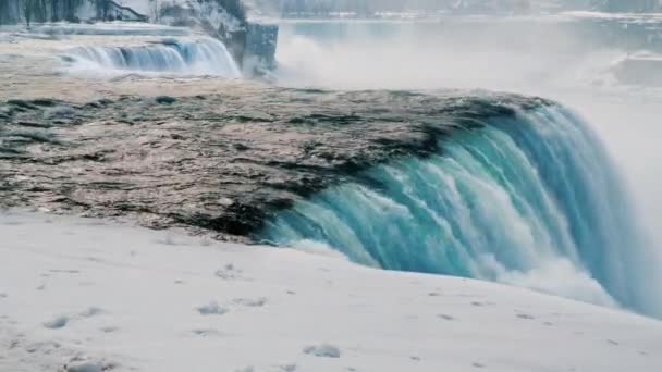 Vista desde el lado americano hasta las cataratas del Niágara de invierno. Tierra cubierta de nieve en primer plano — Vídeos de Stock