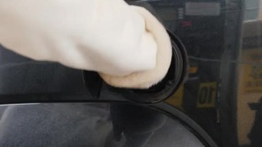 Kış giysileri içinde bir kadın arabasını çalıştırır. Yakıt tankı kapağı açar ve yakıt ikmal silah ekler