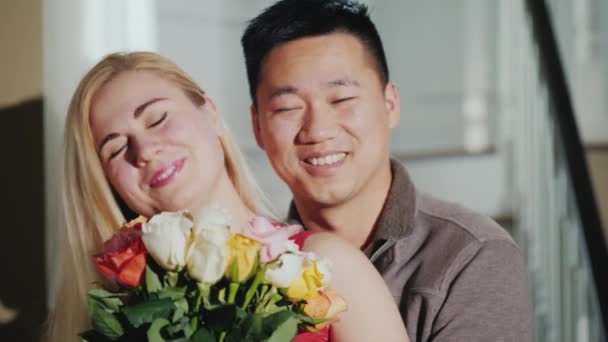 Joyeux jeune couple avec un bouquet de fleurs. Souriant, regardant la caméra. Asiatique homme et caucasien femme — Video