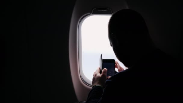 Силует чоловіка, який фотографує з вікна літака, дивиться з вікна — стокове відео