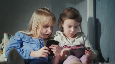 İki kız akıllı telefonlar üzerinde oynamak. Yatak yatakta yan yana oturmak
