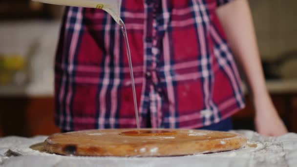 Egy nő önti a növényi olaj a deszkán, ahol ő kezd dagasztani a tésztát a pizza — Stock videók