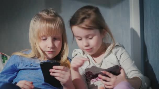 Две забавные девушки играют на своих смартфонах, обсуждают новые элементы в игровых приложениях — стоковое видео