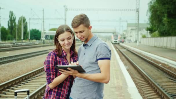 La joven pareja feliz viaja en tren. Párate en la estación, usa una tableta — Vídeo de stock