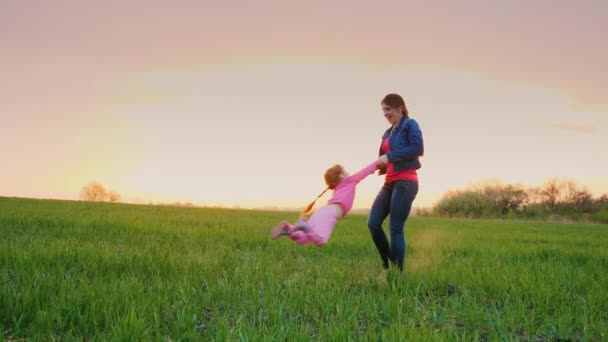 Jovem mamãe está brincando com sua filha em um lugar pitoresco. Circula-a à volta dele, ao pôr do sol. — Vídeo de Stock