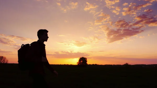 Een tiener met een rugzak over zijn schouder gaat naar de zonsondergang in het veld of op het platteland. Silhouet video, zijaanzicht. Concept - nieuwe onderzoek, vooruit naar het onbekende, naar het huis te verlaten — Stockfoto