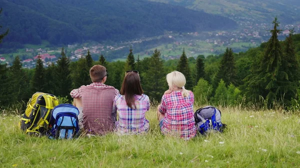 Amigos de turistas sentam-se em um lugar pitoresco no fundo das montanhas. Descansam, admiram a bela paisagem — Fotografia de Stock