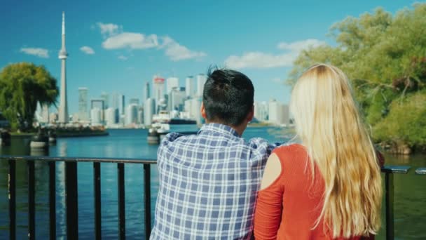 Молодая многонациональная пара смотрит на прекрасный вид на город Торонто. Вид сзади. Концепция путешествия по Канаде — стоковое видео