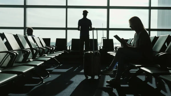 La gente al terminal dell'aeroporto sta aspettando il volo. Utilizzare dispositivi, guardando attraverso le finestre al campo d'aviazione e aerei — Foto Stock