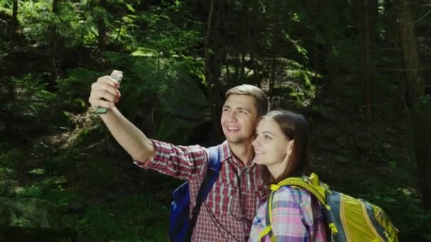 Una atractiva pareja de turistas son fotografiados en el bosque. Selfie con mochilas en una caminata — Vídeos de Stock